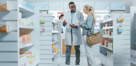 A pharmacist holding a medicine box speaking to a patient in a pharmacy.